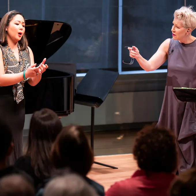Joyce DiDonato gestures to a singing young woman as an audience watches