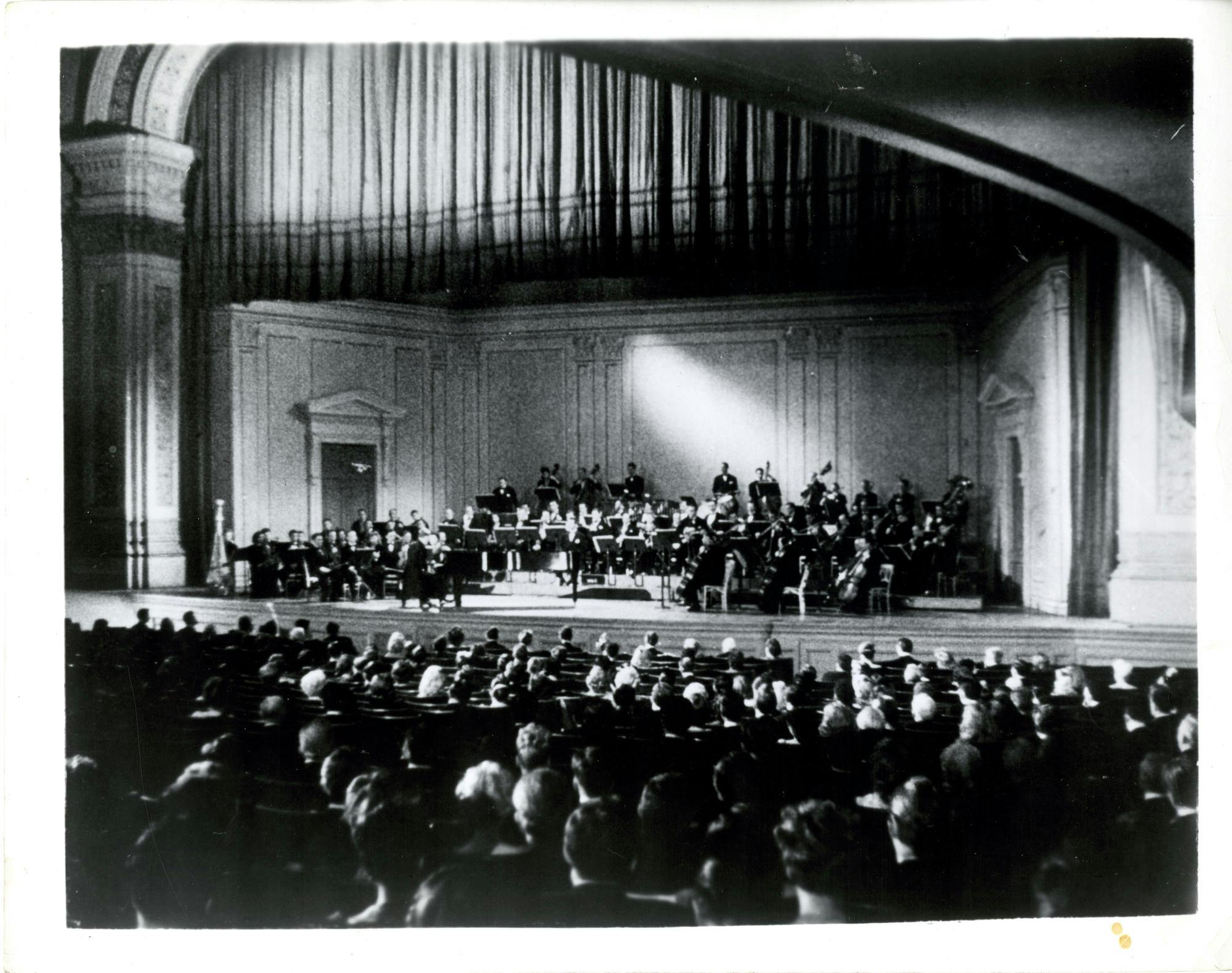 Carnegie Hall’s stage with an orchestra performing beneath a curtain, circa 1940s
