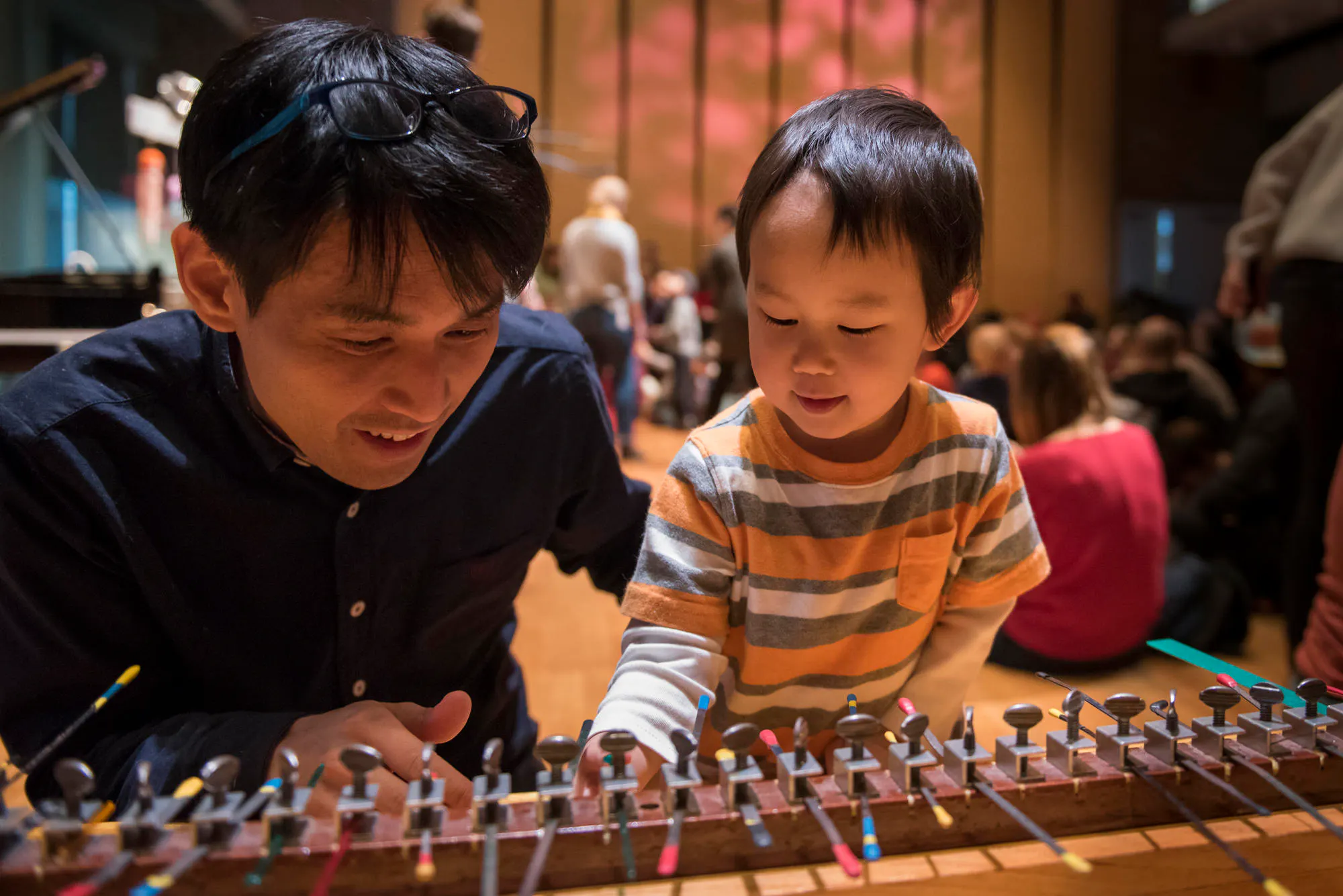 Photo of a father helping his son explore a handmade instrument during a Carnegie Kids event