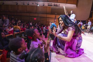 Three Black students wave and give a high five to Falu Shah, who crouches on stage to meet them.