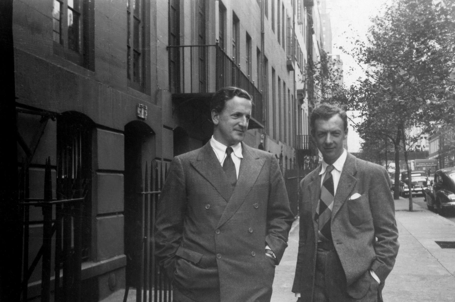 Benjamin Britten with tenor Peter Pears, both wearing suits on an apartment-lined street in Brooklyn