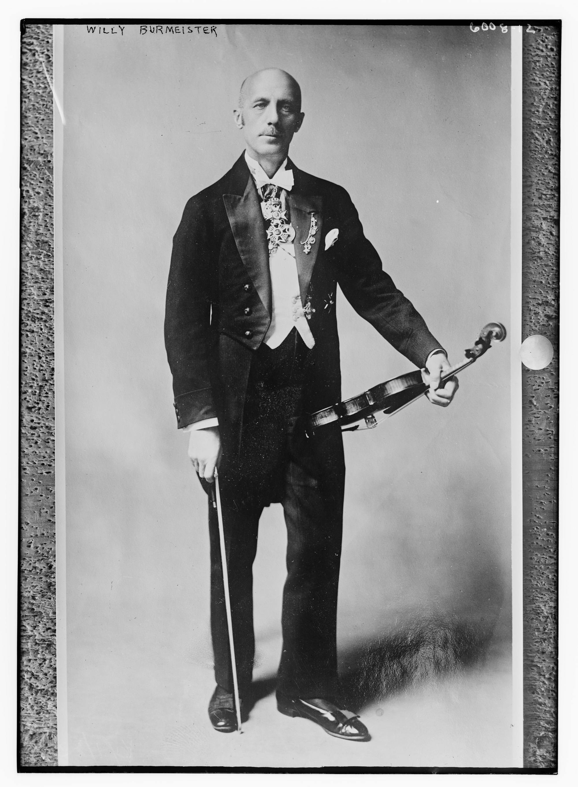 Black-and-white full-body photo of Willy Burmeister wearing a tuxedo and medals, holding his violin
