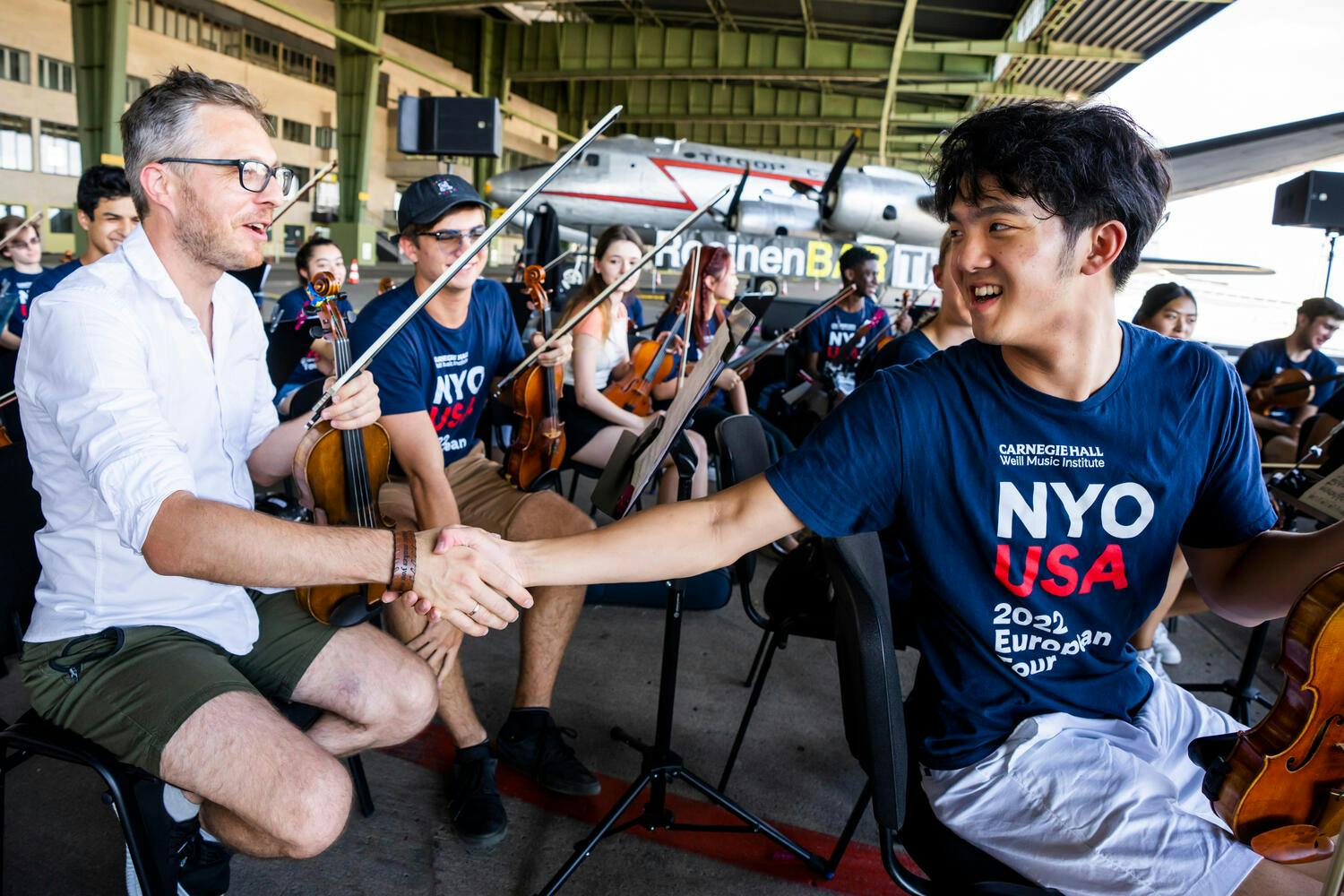 A Ukrainian male violinist shakes hands with a male NYO-USA violinist
