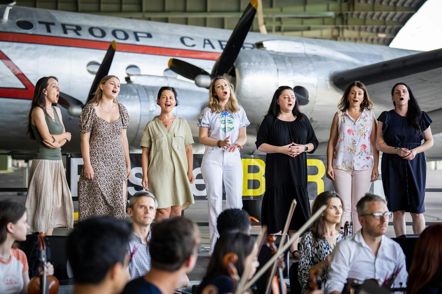 Female Ukrainian singers perform standing in front of an airplane
