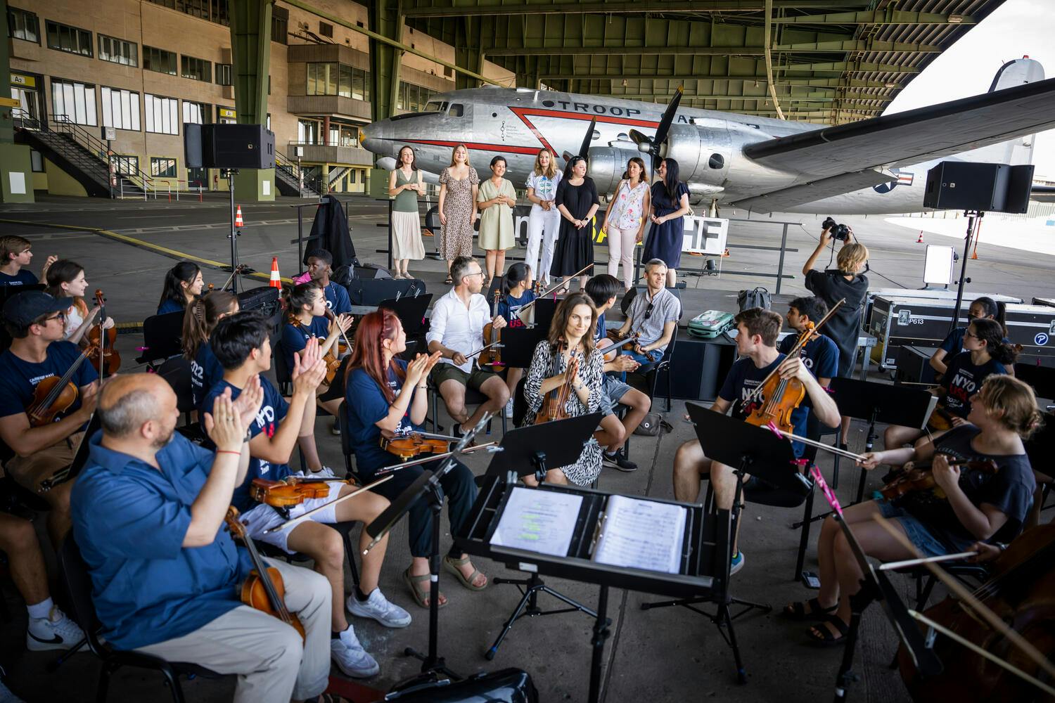Violinists applaud female Ukrainian singers in an airplane hangar