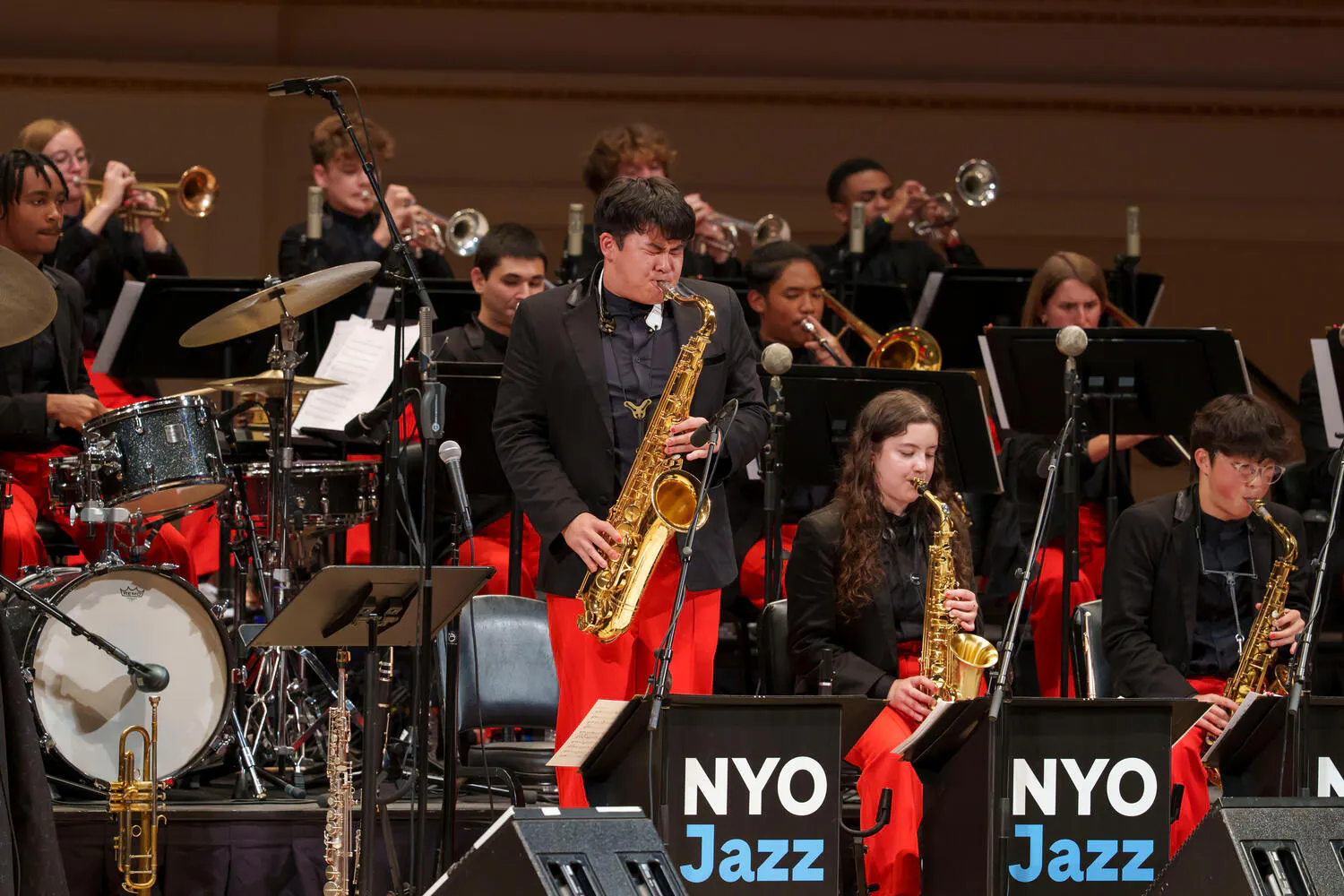 A saxophonist standing up and performing with NYO Jazz on stage