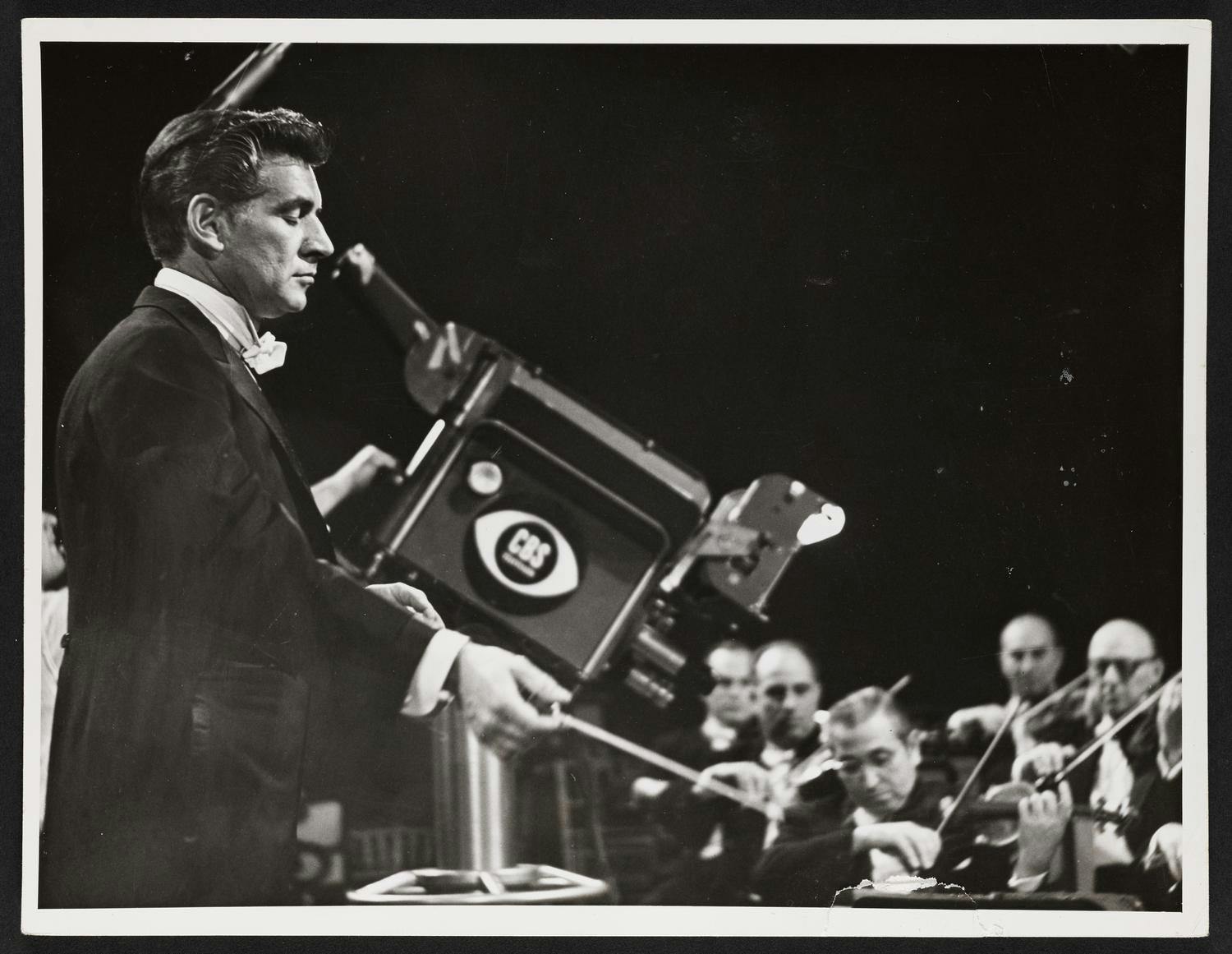 Leonard Bernstein conducting on stage beside a TV camera