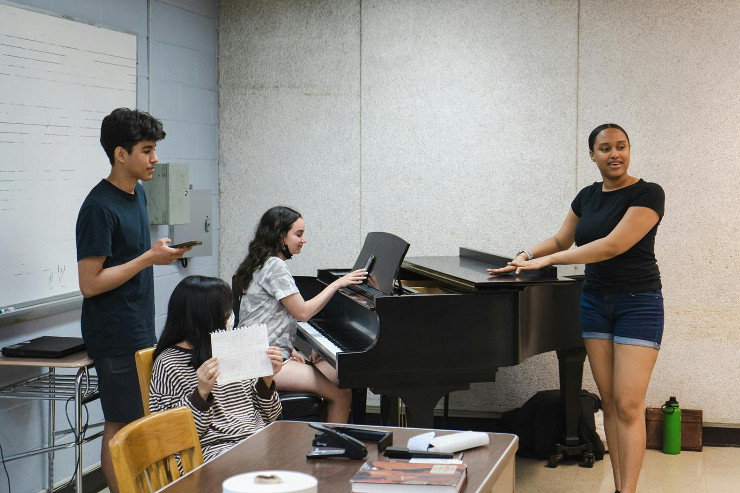A group of young students around the piano in a classroom