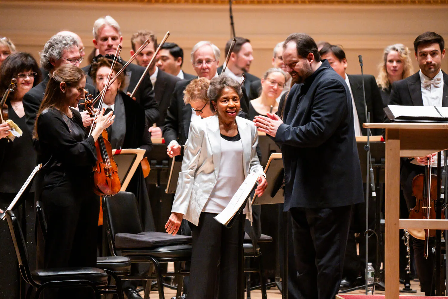 Tania León standing in the middle of the orchestra as the musicians applaud