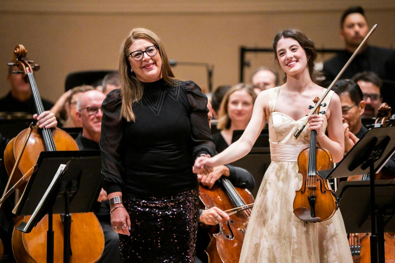 Gabriela Ortiz and María Dueñas holding hands on stage and smiling towards audience.