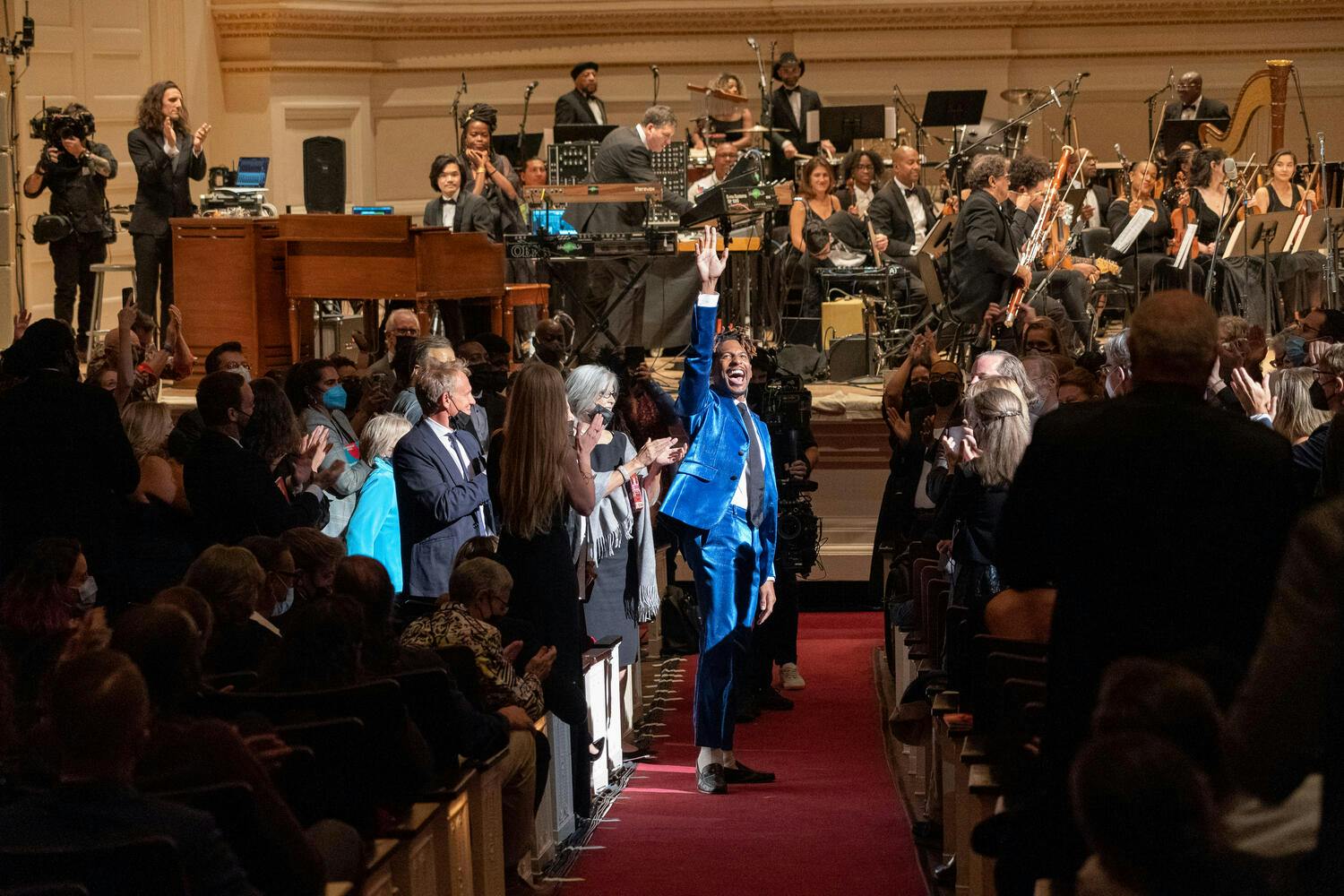 Jon Batiste walking down the aisle, waving to the crowd.