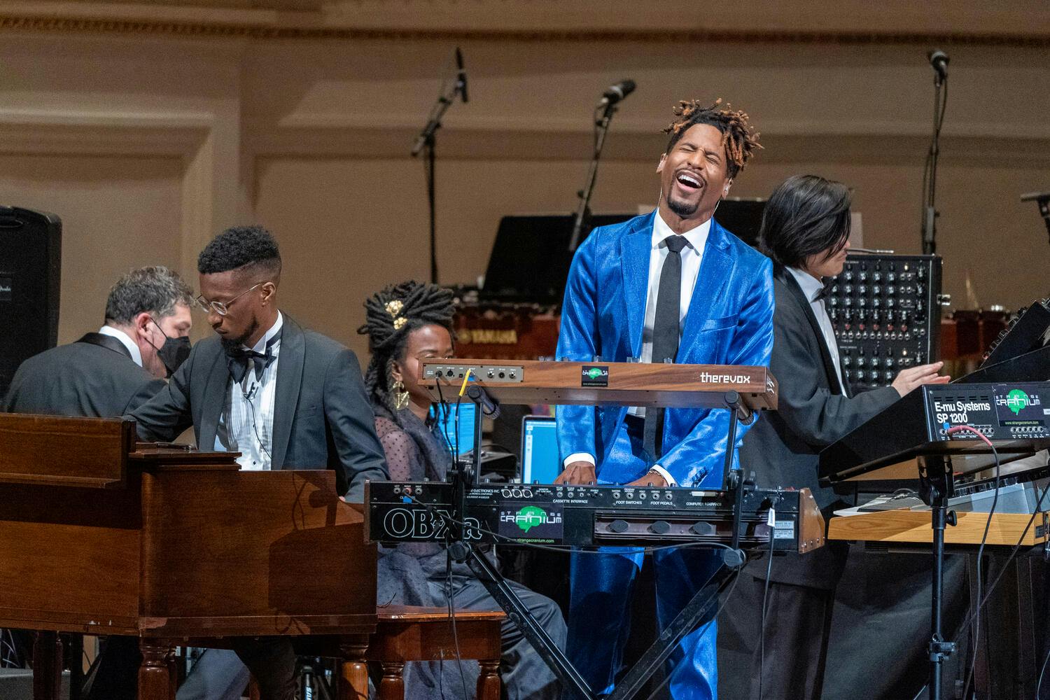 Jon Batiste playing an electric keyboard and singing on stage.