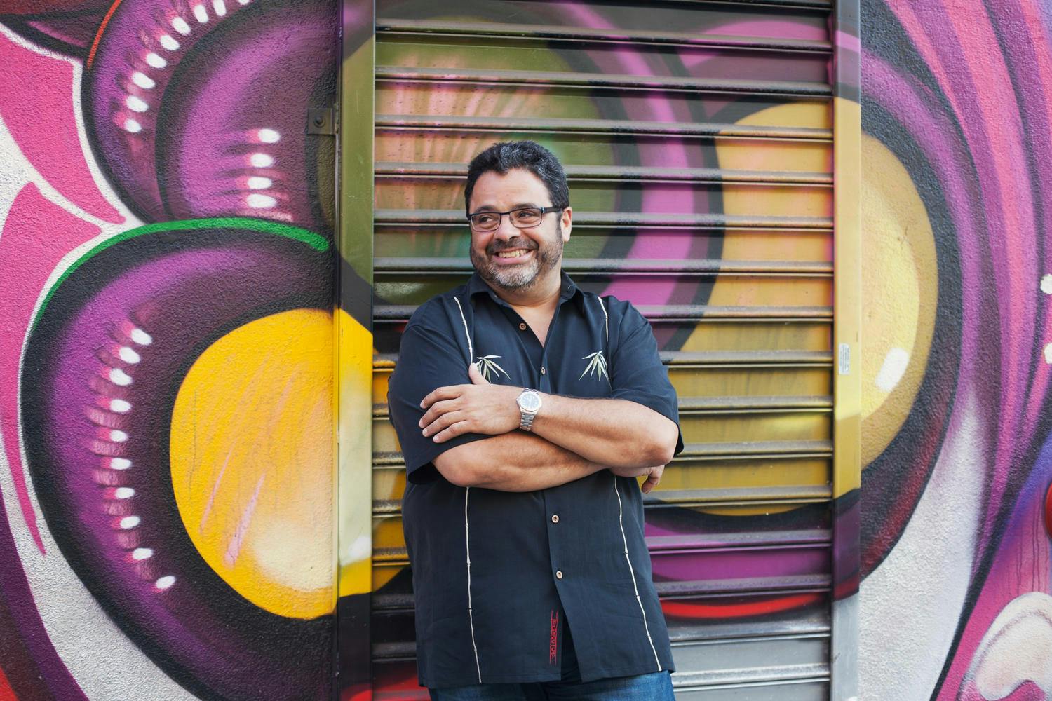  Arturo O’Farrill standing with his arms crossed in front of a mural.