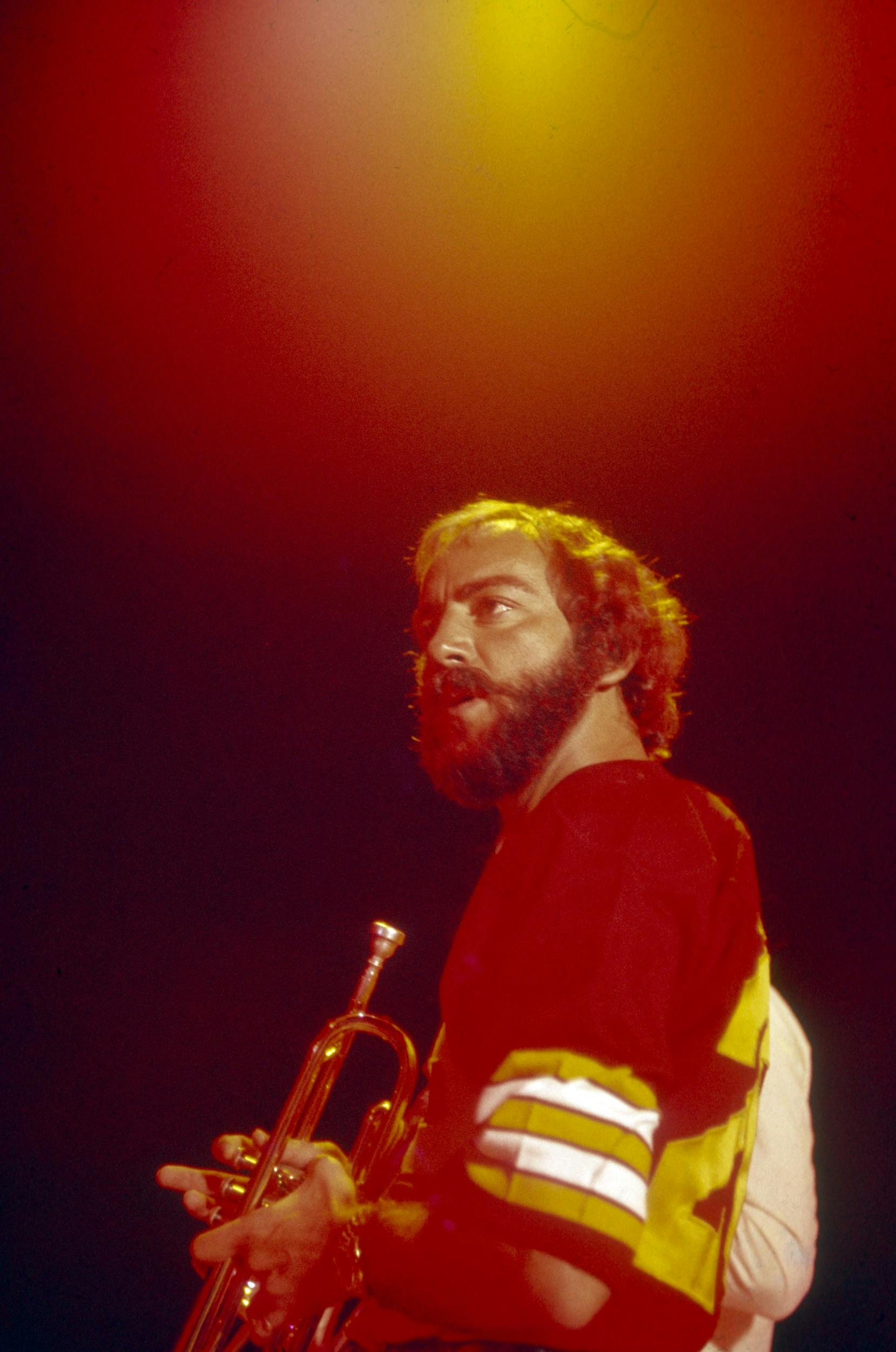 Jerry Masucci performing on stage with a trumpet under stage lighting.