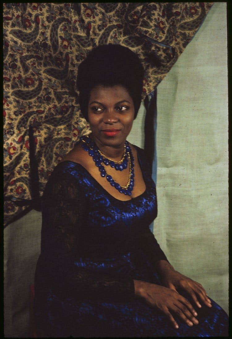 Photo of Armenta Adams wearing a dress and sitting with her hands on her lap.