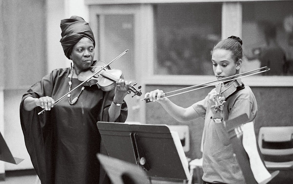 Armenta Adams playing the violin alongside a student.