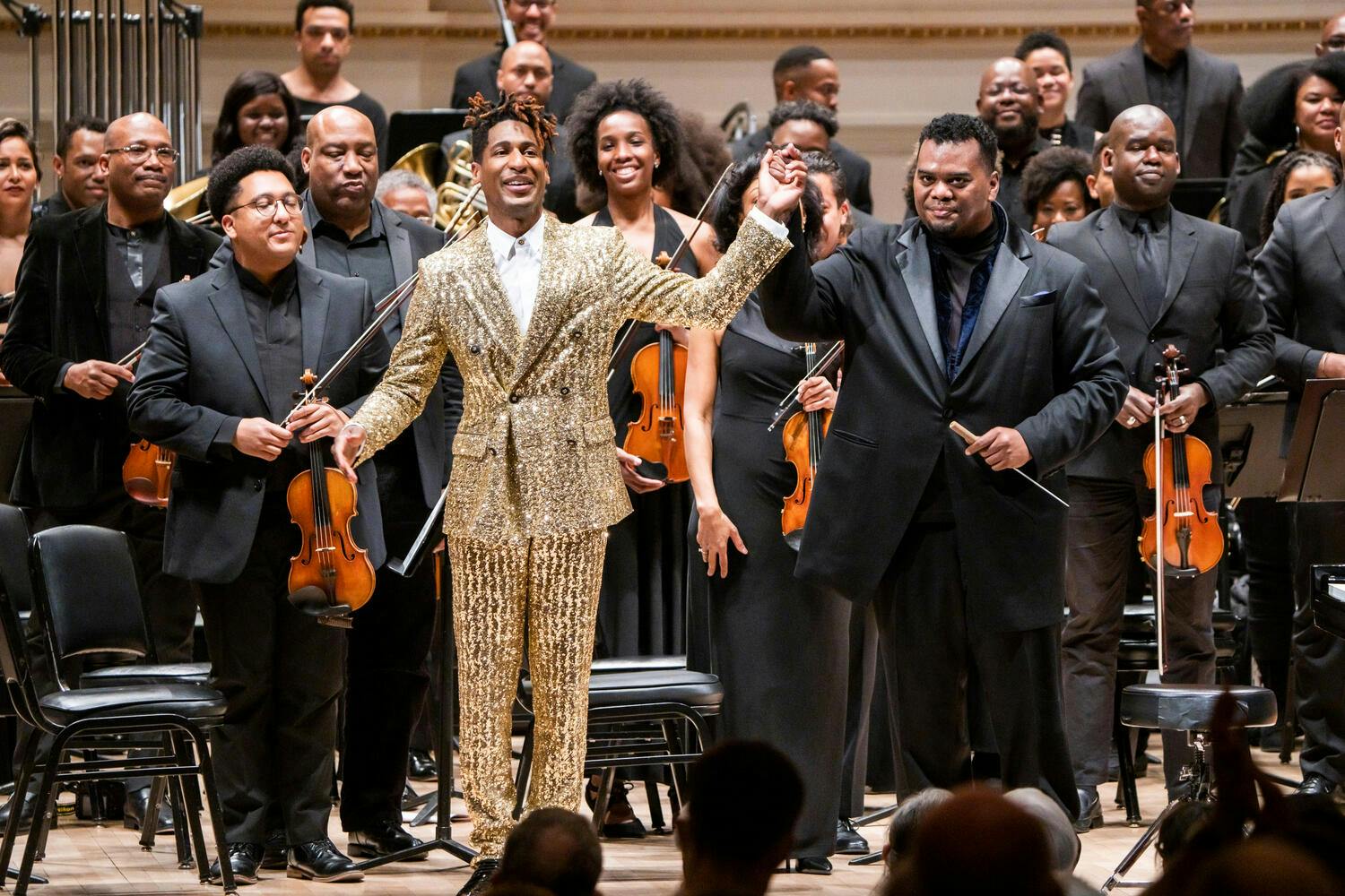 Jon Batiste with conductor Anthony Parnther and the Gateways Festival Orchestra bowing on stage at Carnegie Hall.