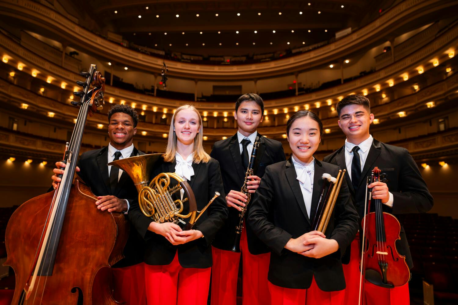 Group of NYO-USA 2024 musicians holding their instruments in Stern Auditorium / Perelman Stage.