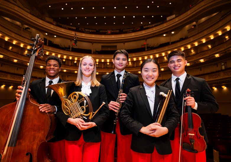Group of NYO-USA 2024 musicians holding their instruments in Stern Auditorium / Perelman Stage.