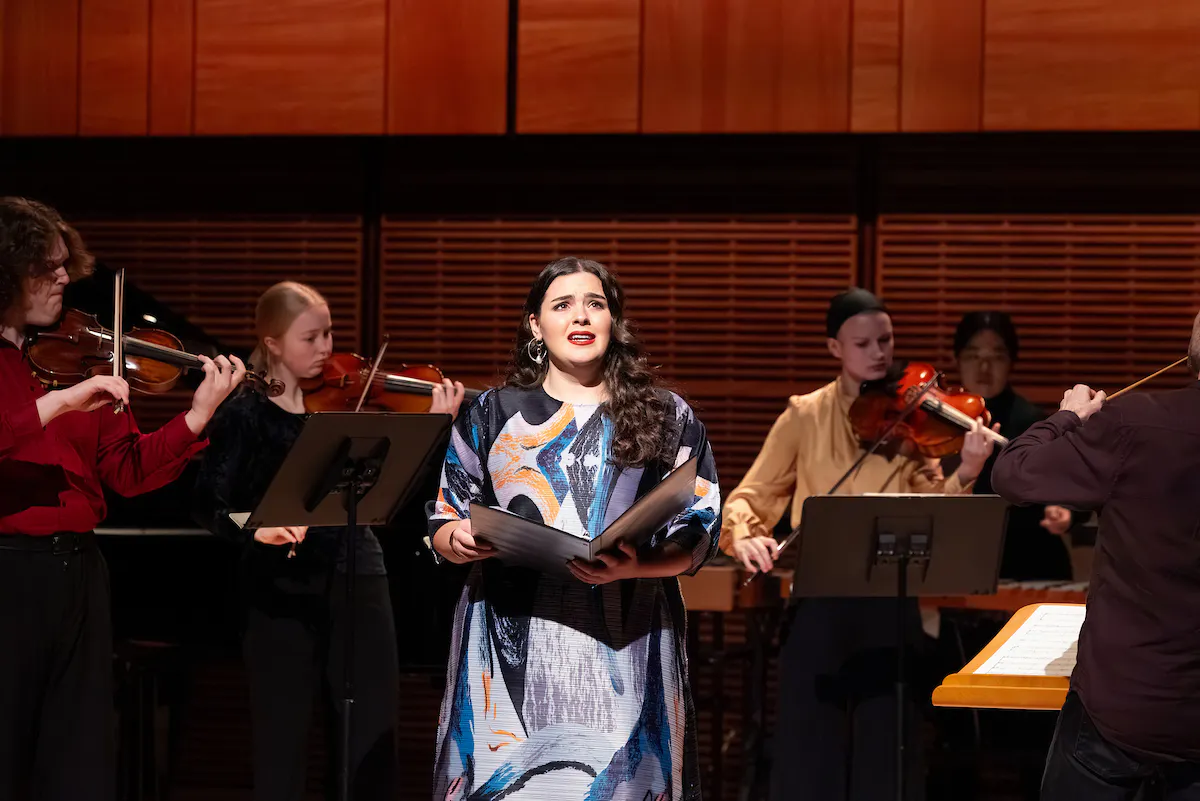 A singer performing while surrounded by string players standing around her on stage in Zankel Hall.