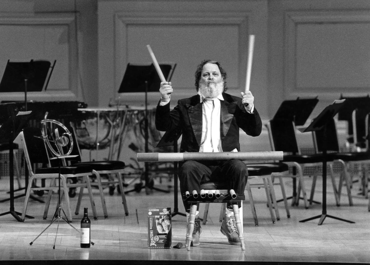 Peter Schickele on stage as P.D.Q. Bach, holding two sticks.