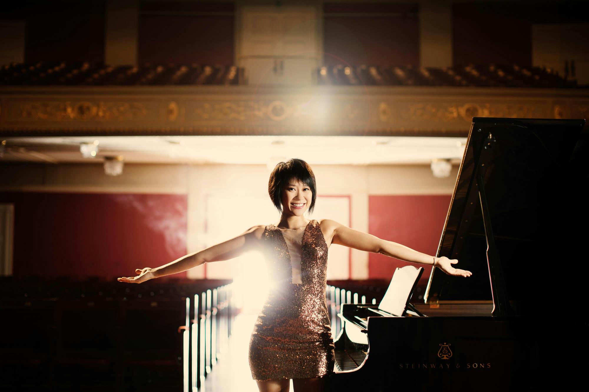 Photo of Yuja Wang standing in front of a piano with her arms extended.