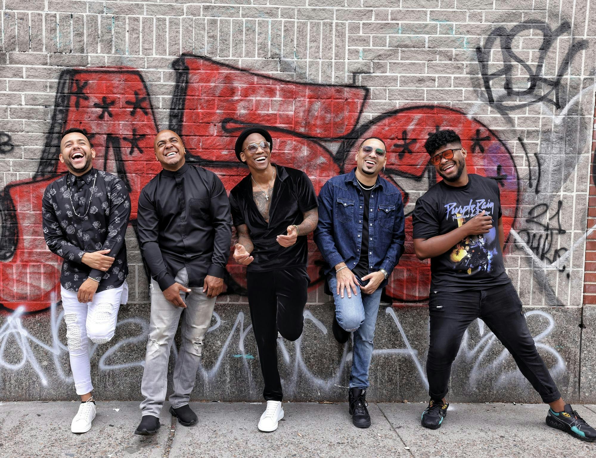 Photo of Pedrito Martinez and members of his band standing in front of a wall of graffiti.