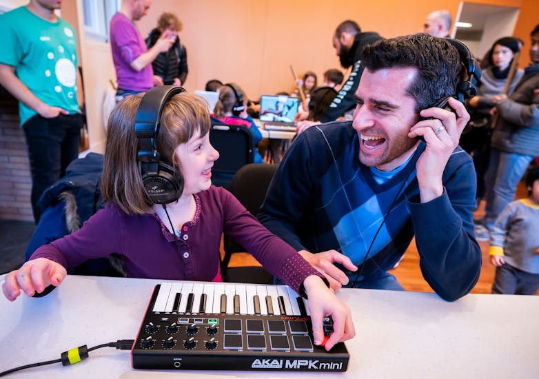 A father-daughter duo wears headphones as they make music on a keyboard