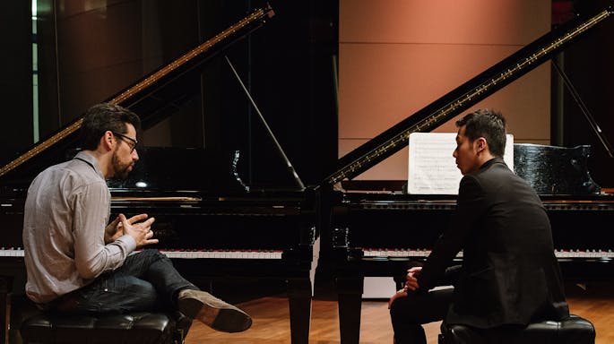 Pianist Jonathan Biss coaches Soohong Park; both men sit in front of pianos, facing each other.