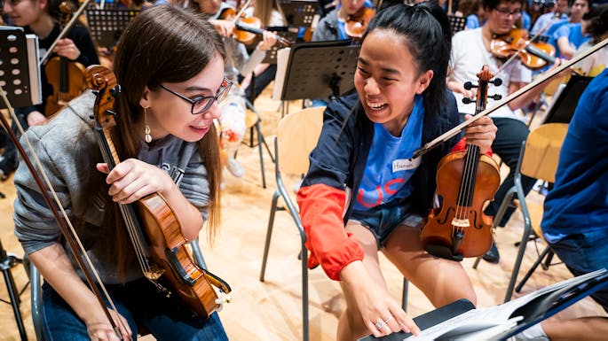Two violinists from NYO-USA and RCO Young share a stand in a joint rehearsal.