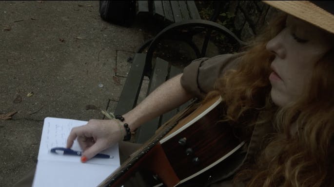 Bridget Barkan sits on a park bench brainstorming with her guitar and notebook.