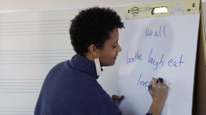 Sarah Elizabeth Charles writes the words “we all breathe, laugh, eat, love” on a large notepad.