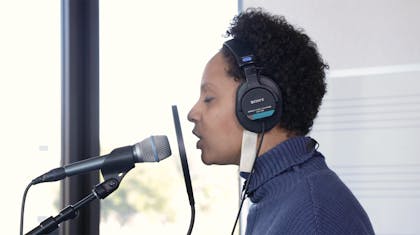 Sarah records her voice on a microphone.
