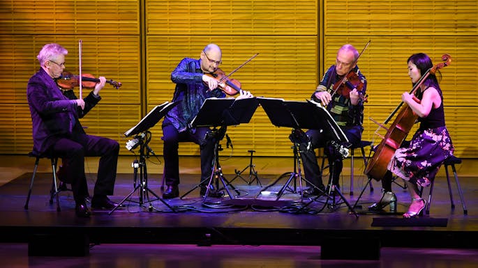 Kronos Quartet performs in Zankel Hall, bathed in contrasting purple and gold light.