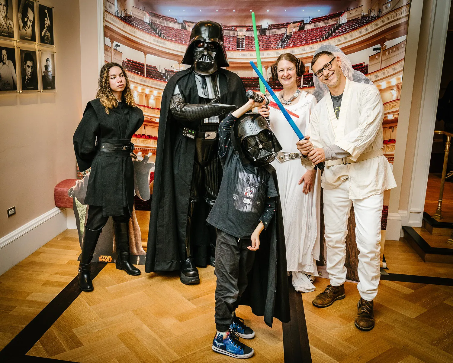 People posing in Star Wars inspired costumes with blue, green, and red lightsabers.