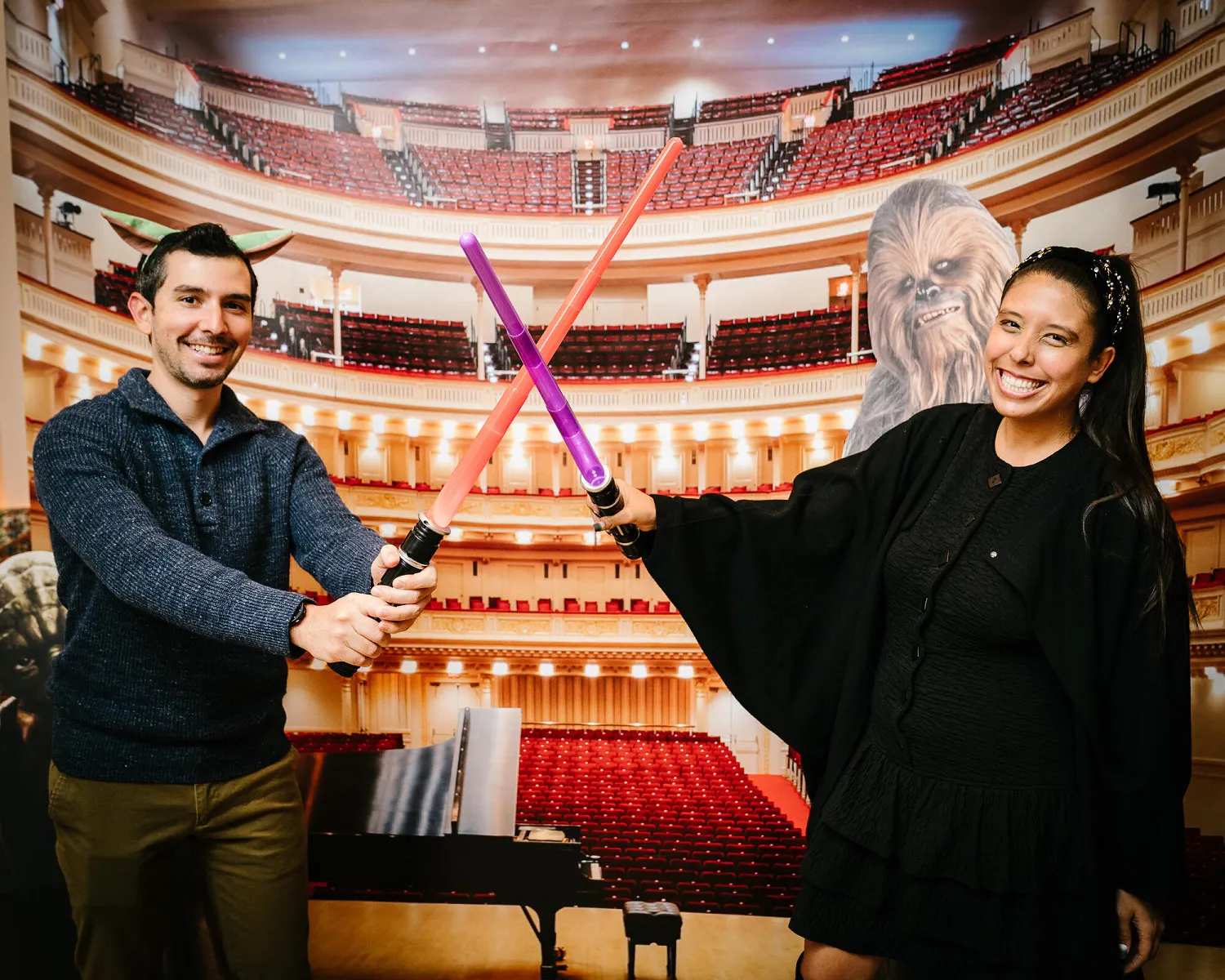 People posing in front of a Carnegie Hall backdrop with red and purple lightsabers.