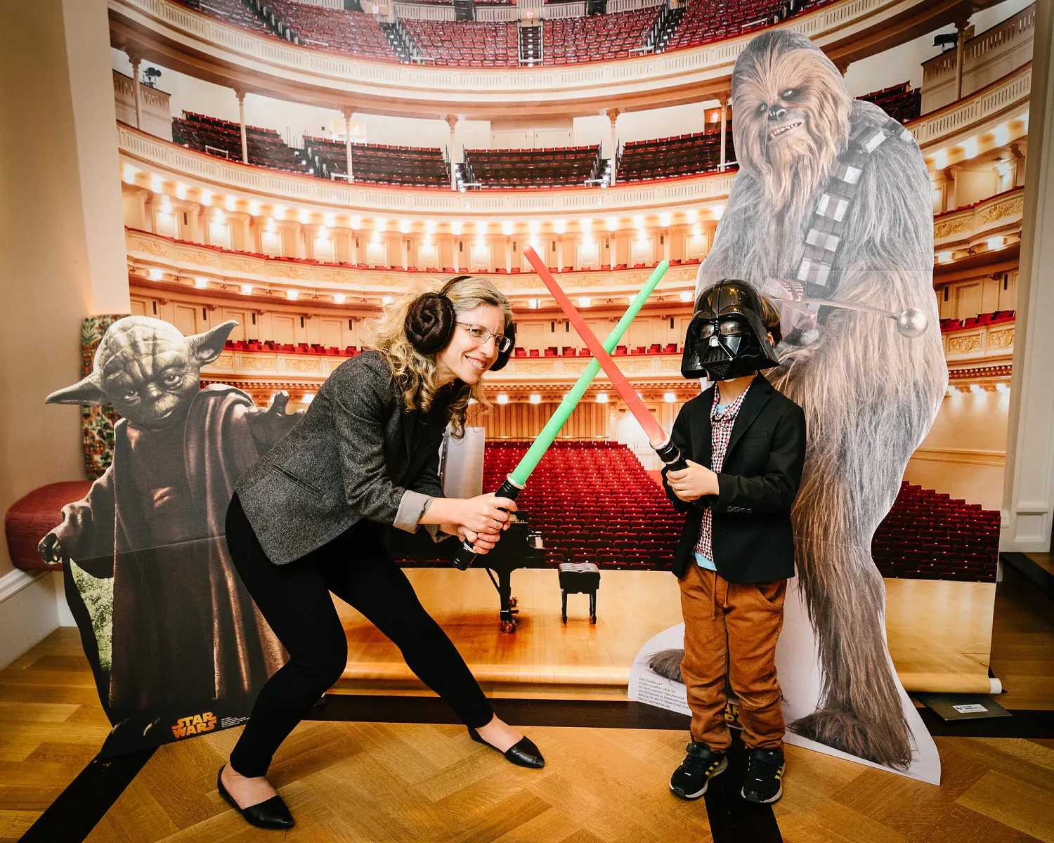 A woman and boy pose with Star Wars character cutouts holding green and red light sabers.