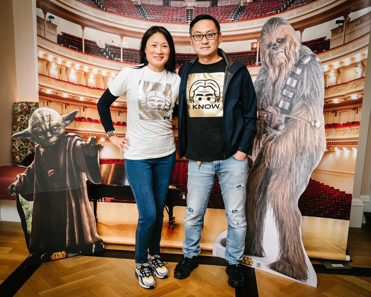 A couple pose in front of a Carnegie Hall backdrop with Star Wars characters beside them.