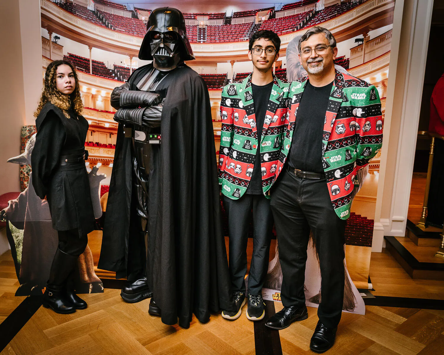 Two men in green and red jackets pose alongside Star Wars characters.