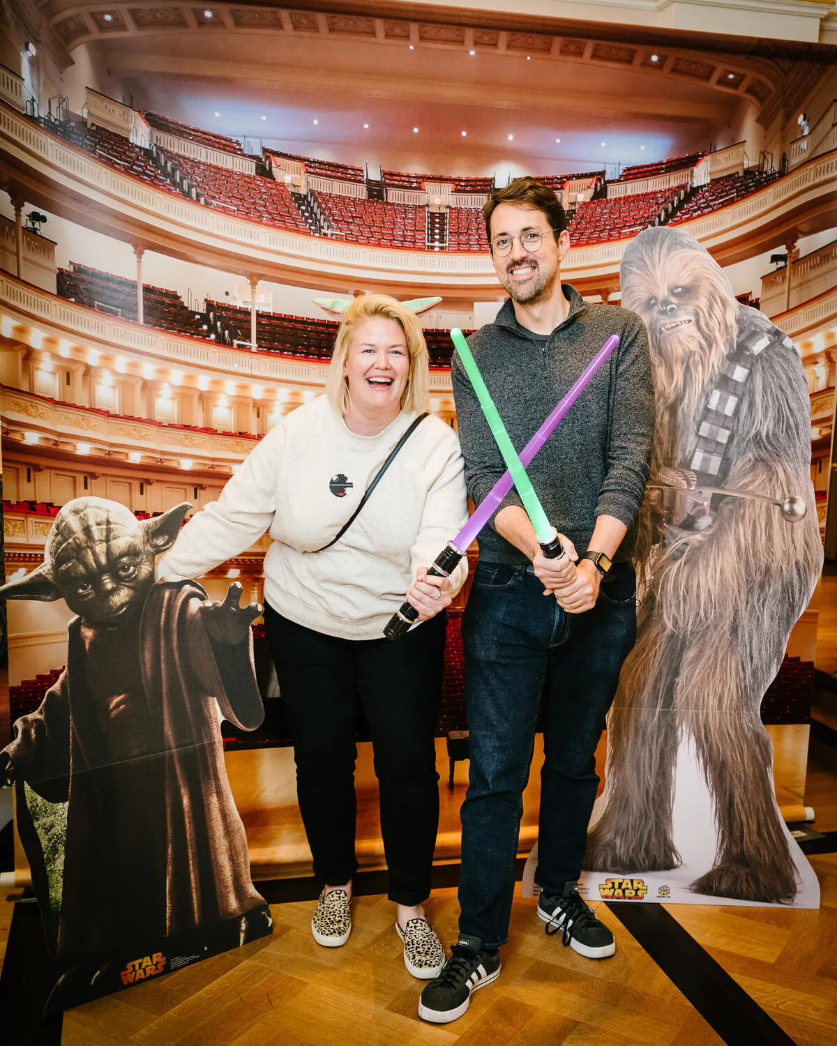 People posing in front of a Carnegie Hall backdrop with green and purple light sabers.
