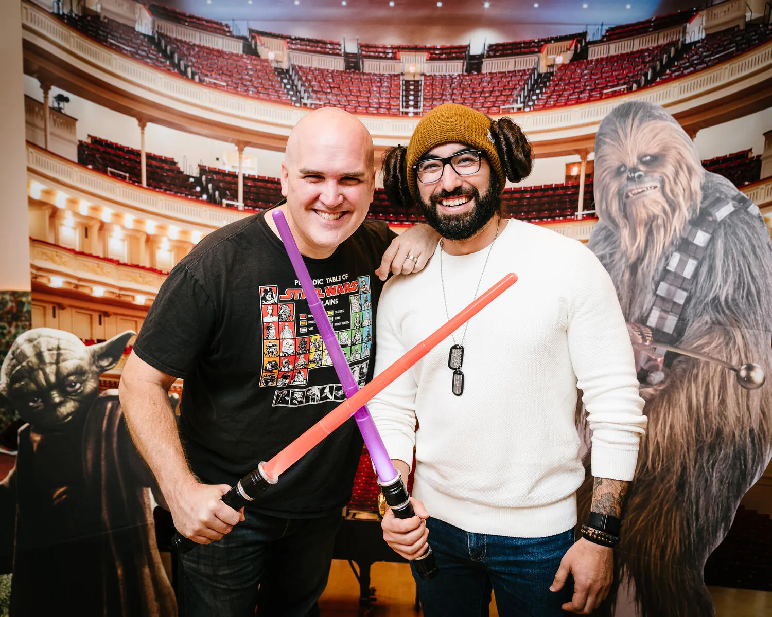 People posing in front of a Carnegie Hall backdrop with red and purple lightsabers.
