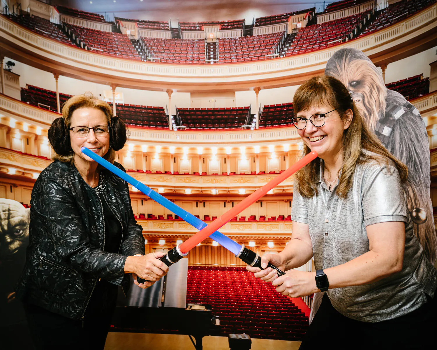 People posing in front of a Carnegie Hall backdrop with red and blue lightsabers.