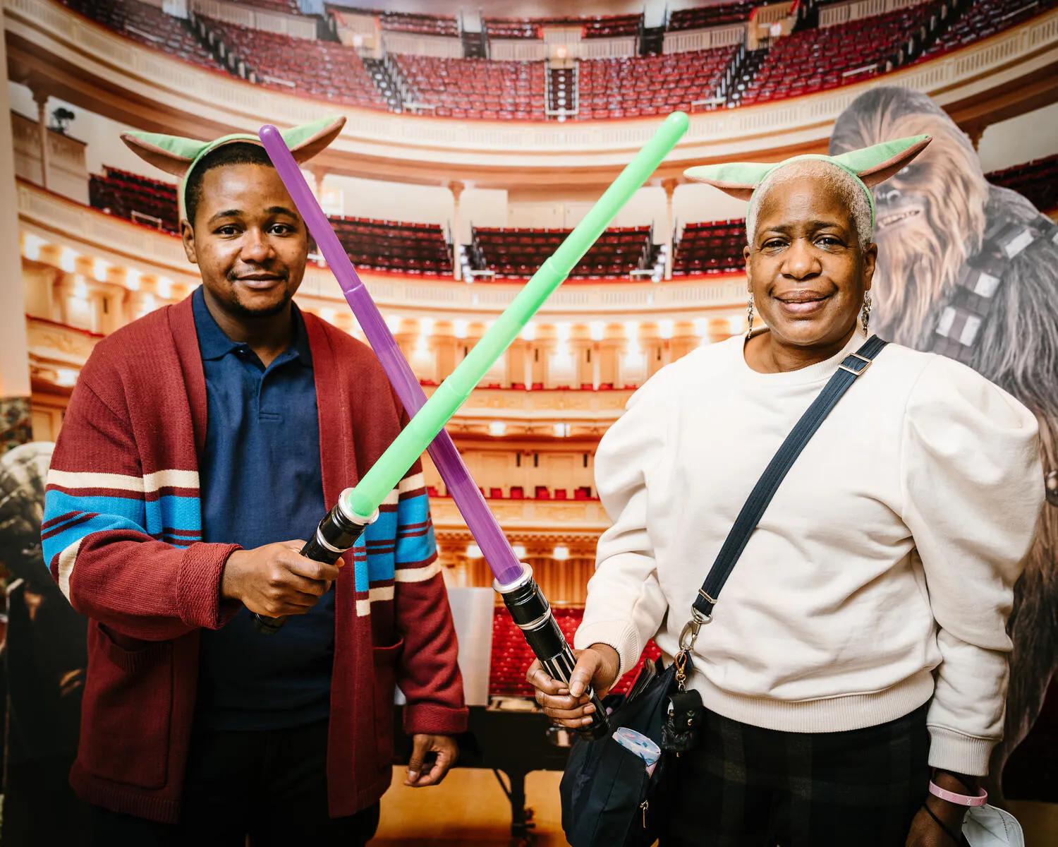 People posing in front of a Carnegie Hall backdrop with green and purple lightsabers.