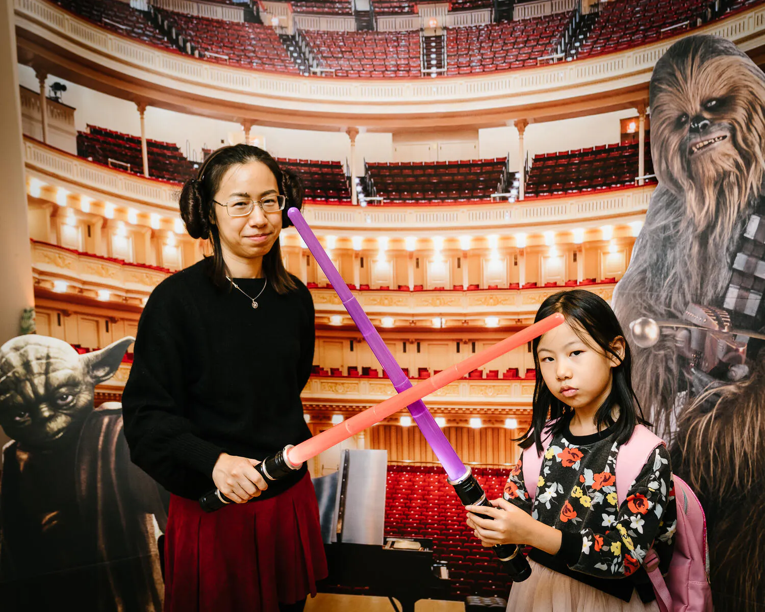 People posing in front of a Carnegie Hall backdrop with red and purple lightsabers.
