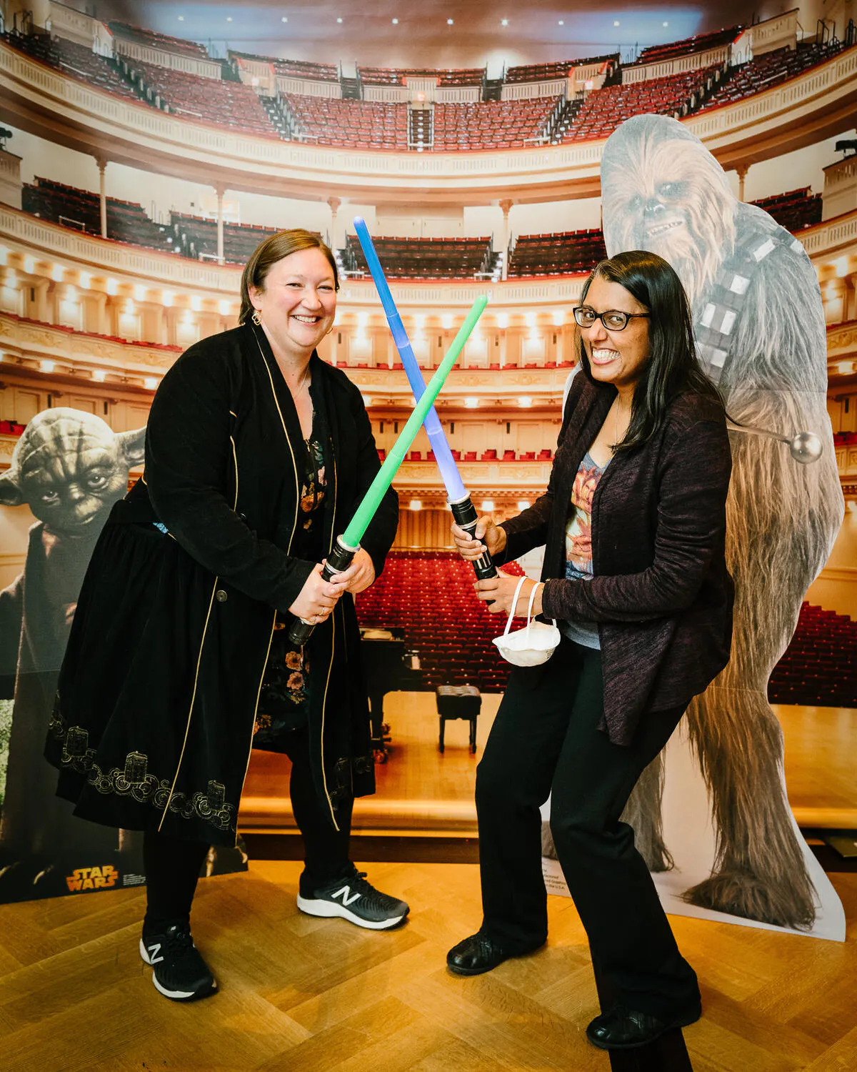 People posing in front of a Carnegie Hall backdrop with green and blue lightsabers.