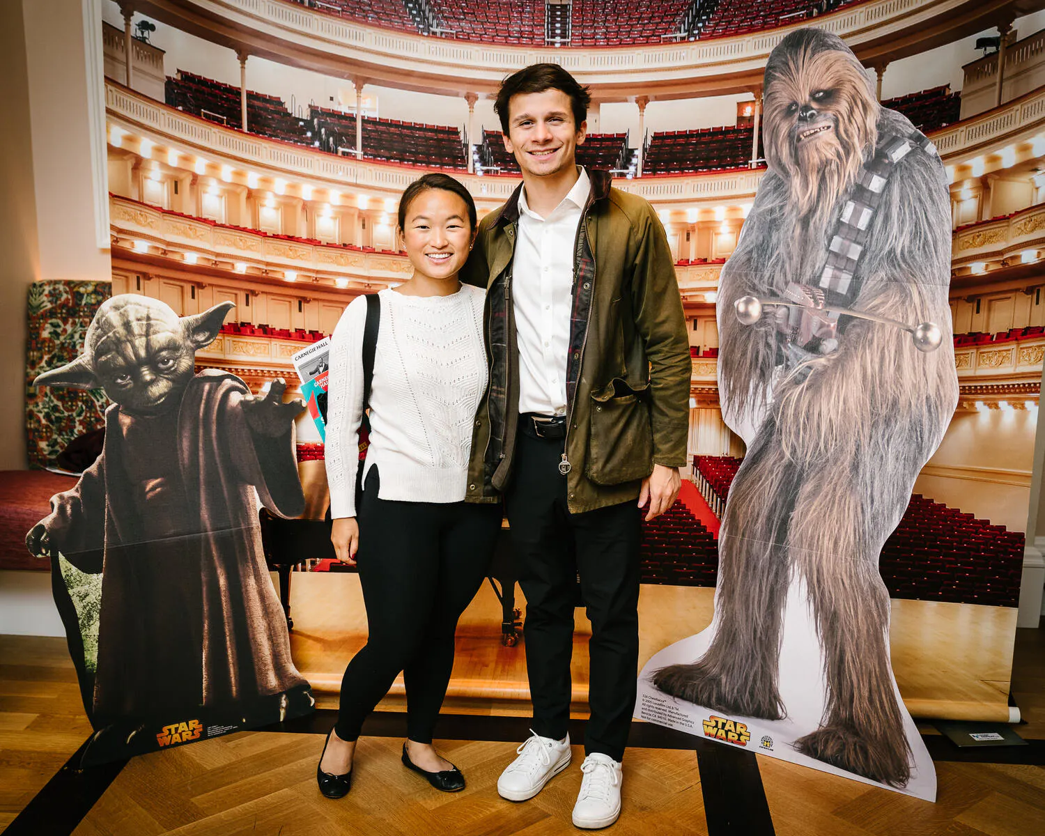 People posing against a backdrop of Carnegie Hall with Star Wars characters beside them.