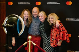 Four people stand in front of a step and repeat and have their picture taken