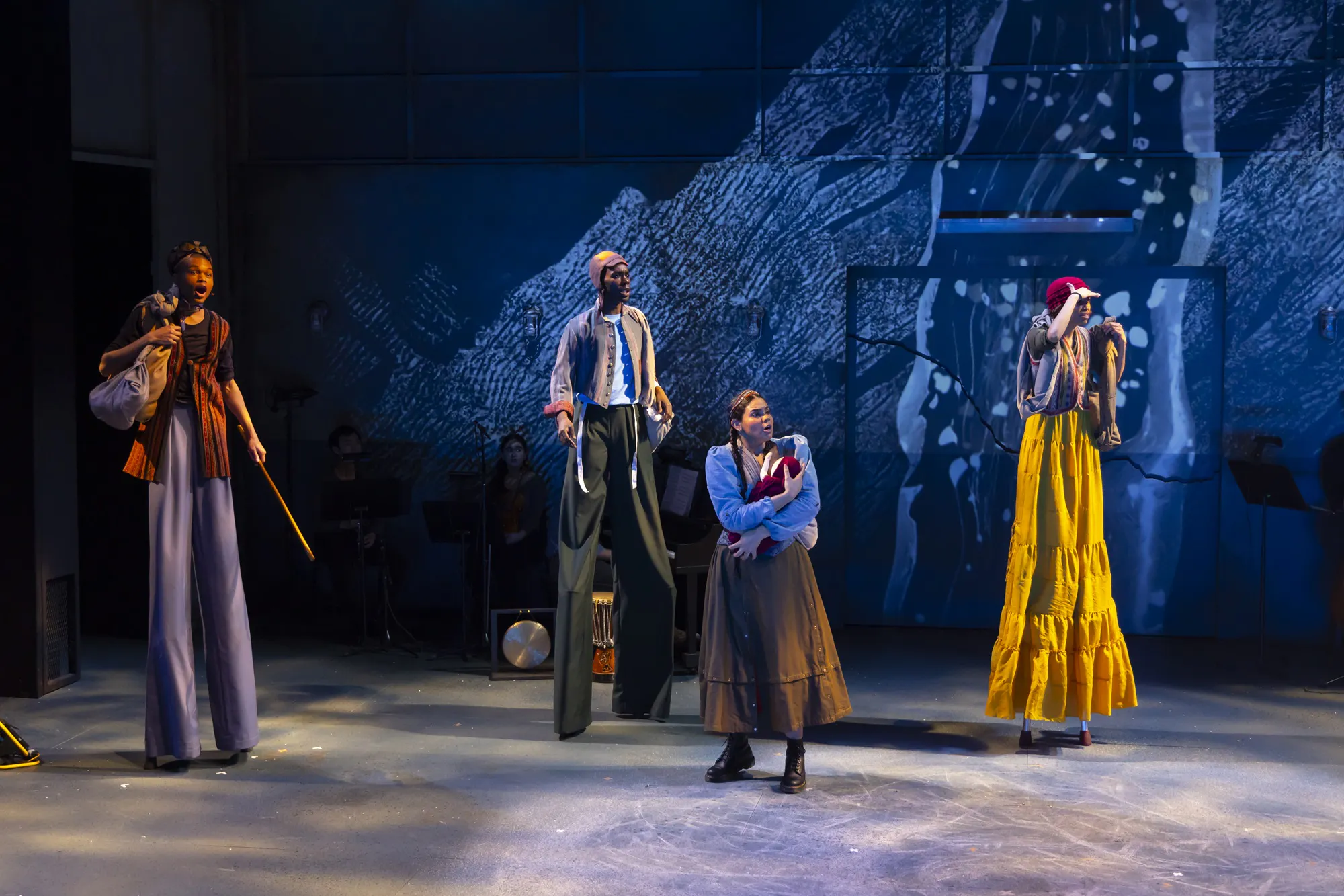 Four performers on stage, three of them on stilts