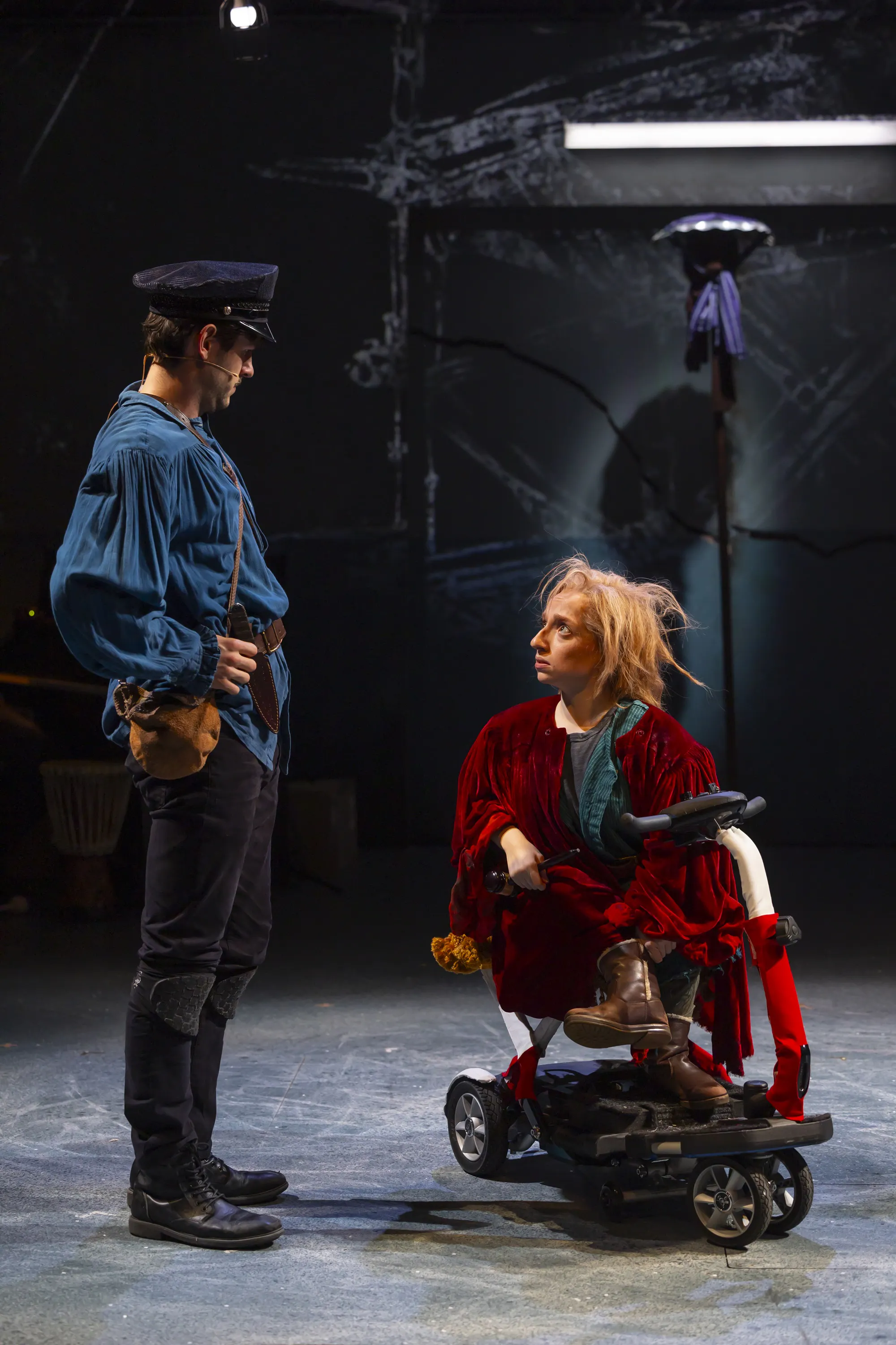 A performer standing, looking at another performer sitting in a wheelchair