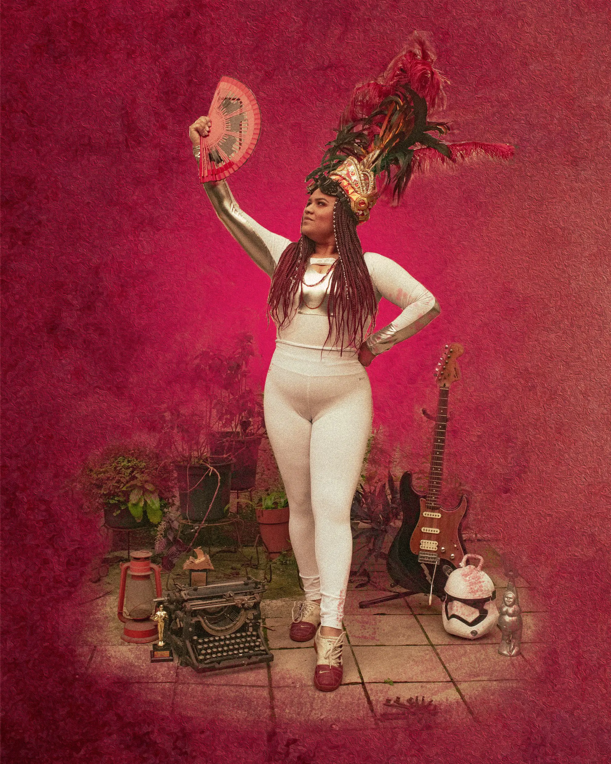 A Carnaval performer holding a far in the air, with several objects placed on the ground including a guitar, lanter, and typewriter